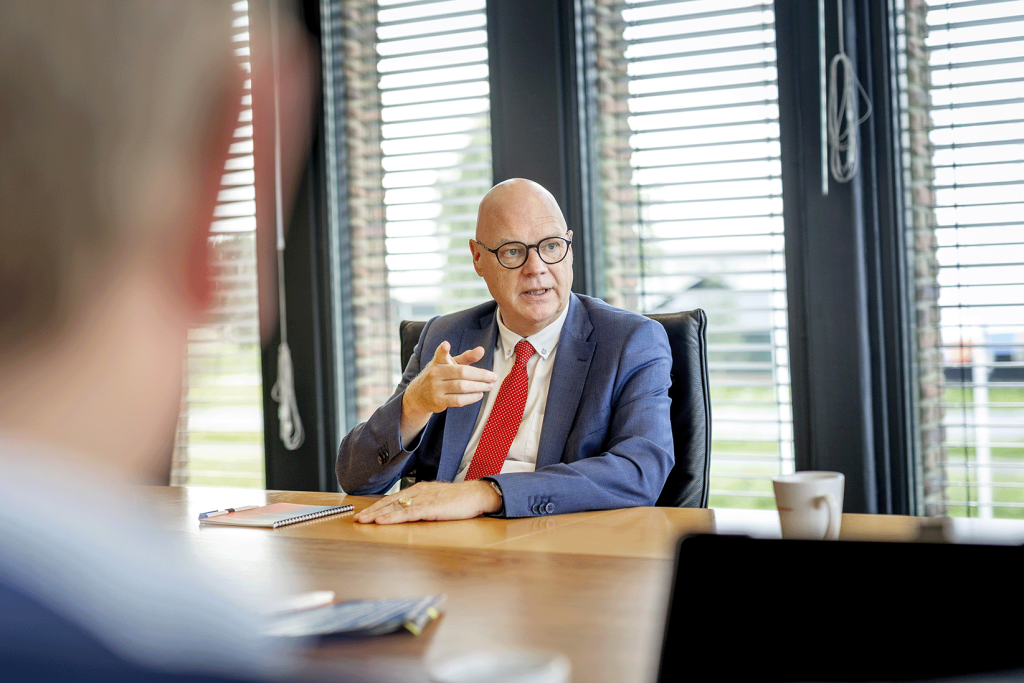 Directeur Nico Wagenvoort zit aan tafel tijdens een vergadering en wijst naar de overkant van de tafel.